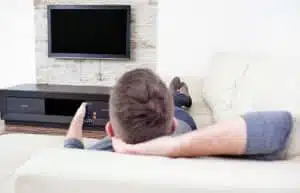 Man relaxing on sofa watching television at home.