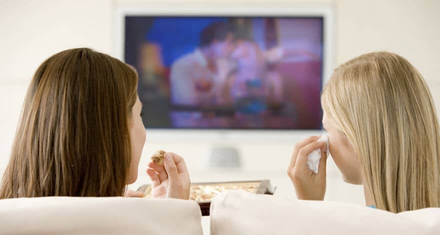 Two women watching a movie and eating pizza.